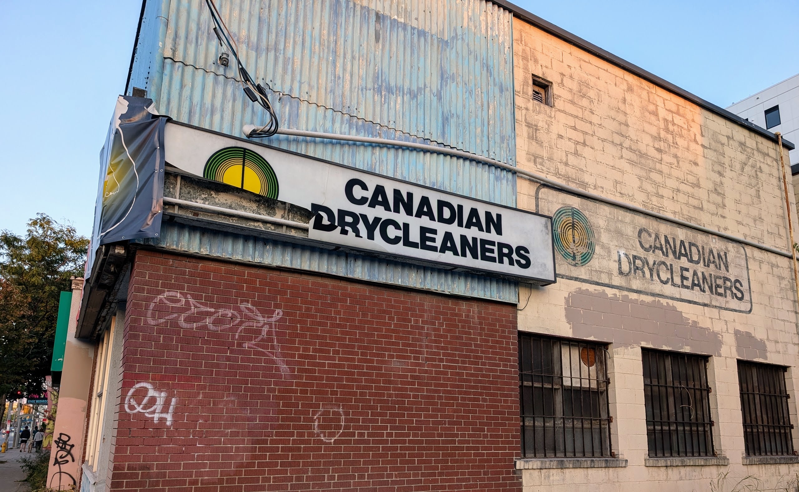 Canadian Drycleaners sign on side of building, including a ghost sign on the bricks, in sept 2025.  The ghost sign has since been painted over.