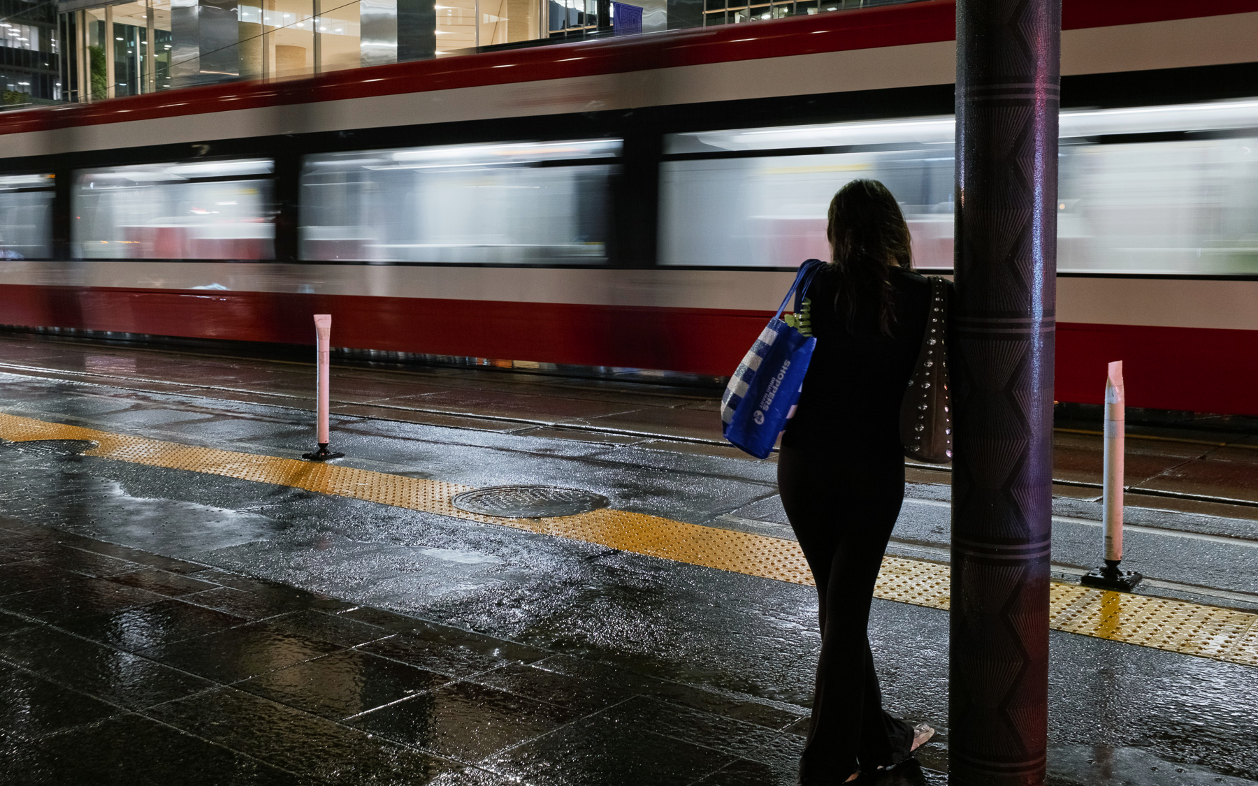 a woman leans against a pole waiting for a streetcar to come during a downpour.  1/2 second exposure, handheld, which blurred the streetcar passing in the other direction.  The camera is water resistant, luckily.